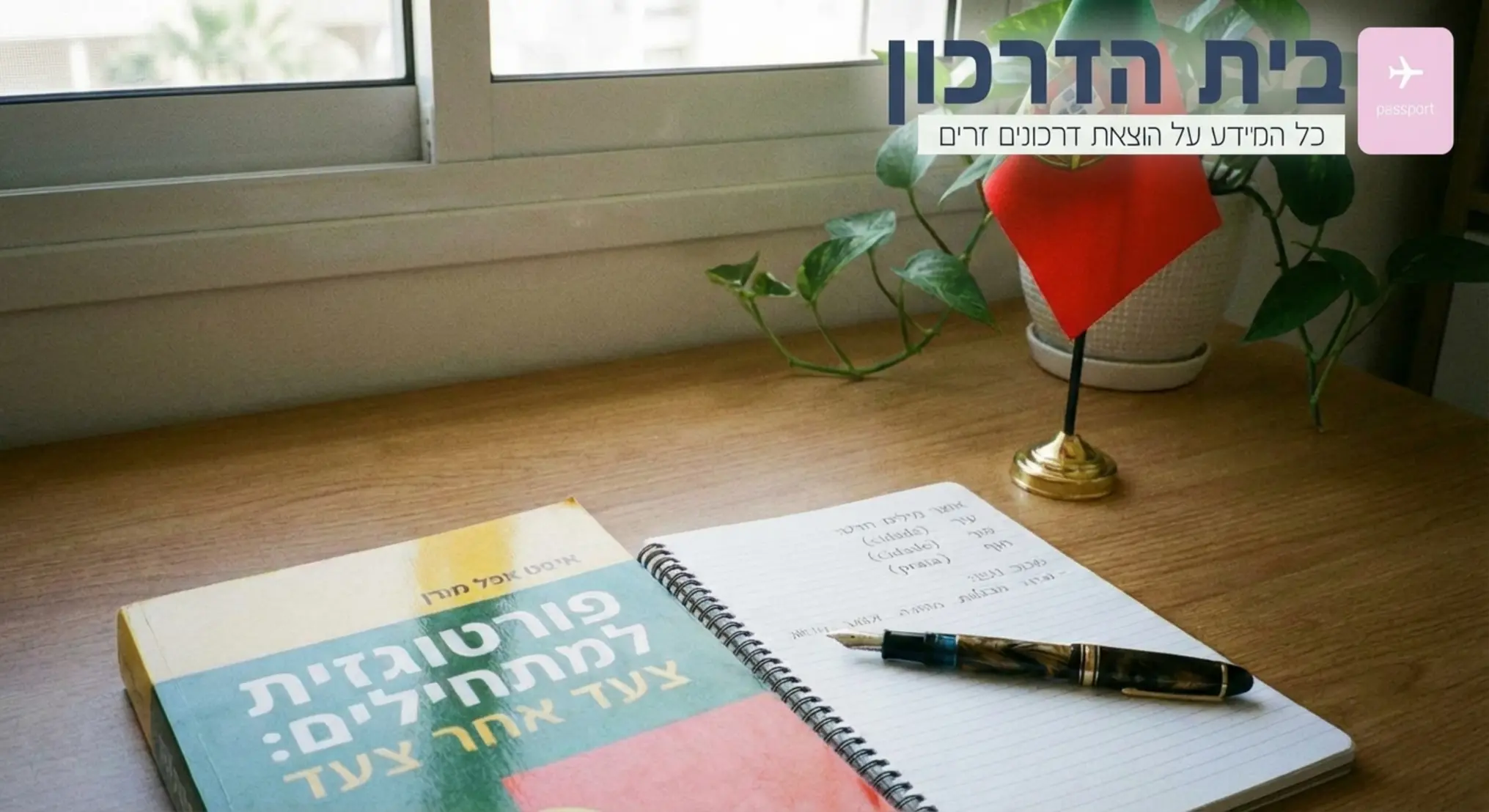 תמונה של שולחן עבודה מסודר עם ספר לימוד פורטוגזית, מחברת פתוחה, עט יוקרתי ודגל קטן של פורטוגל